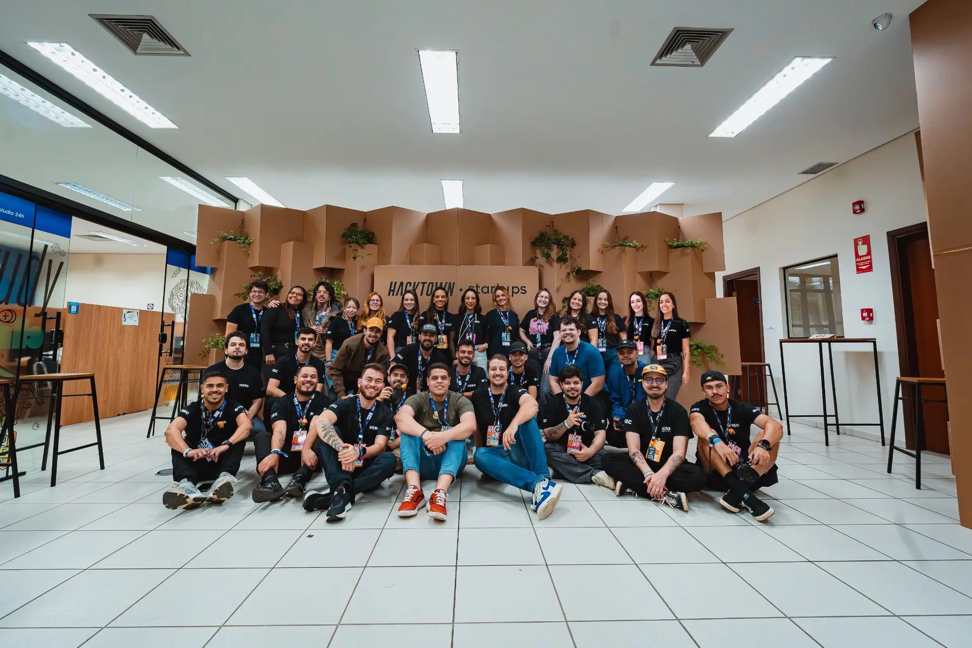 Grupo de pessoas em evento colaborativo em frente à parede decorada com a marca HACKTOWN